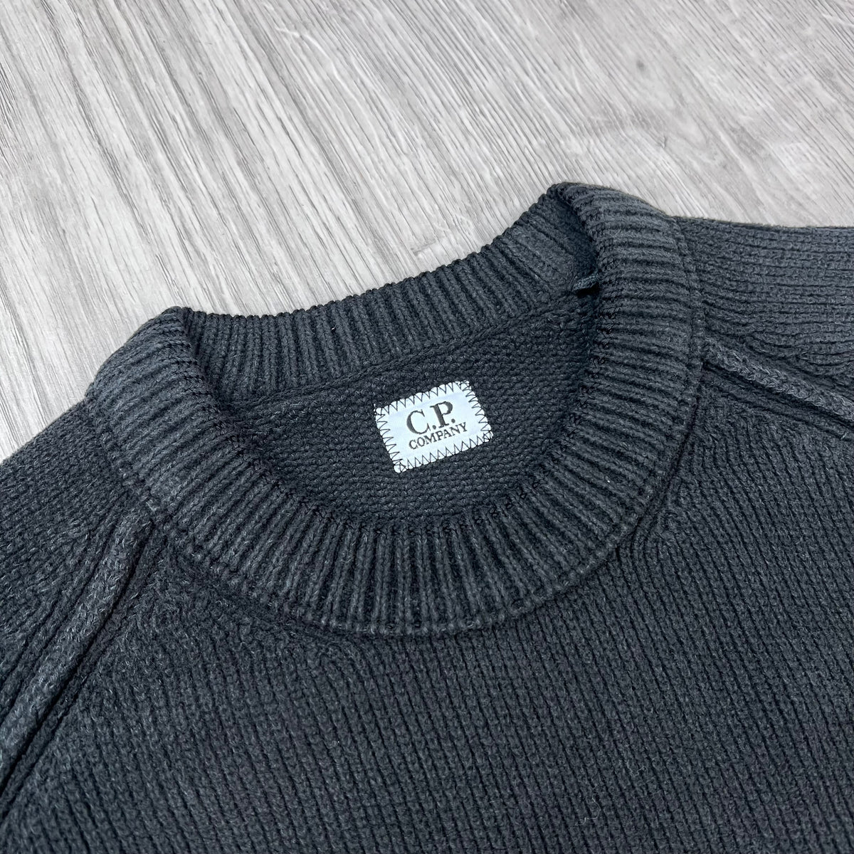 A close view of the crewneck collar on a CP Company Chenille Cotton Lens Sweatshirt in Black. 